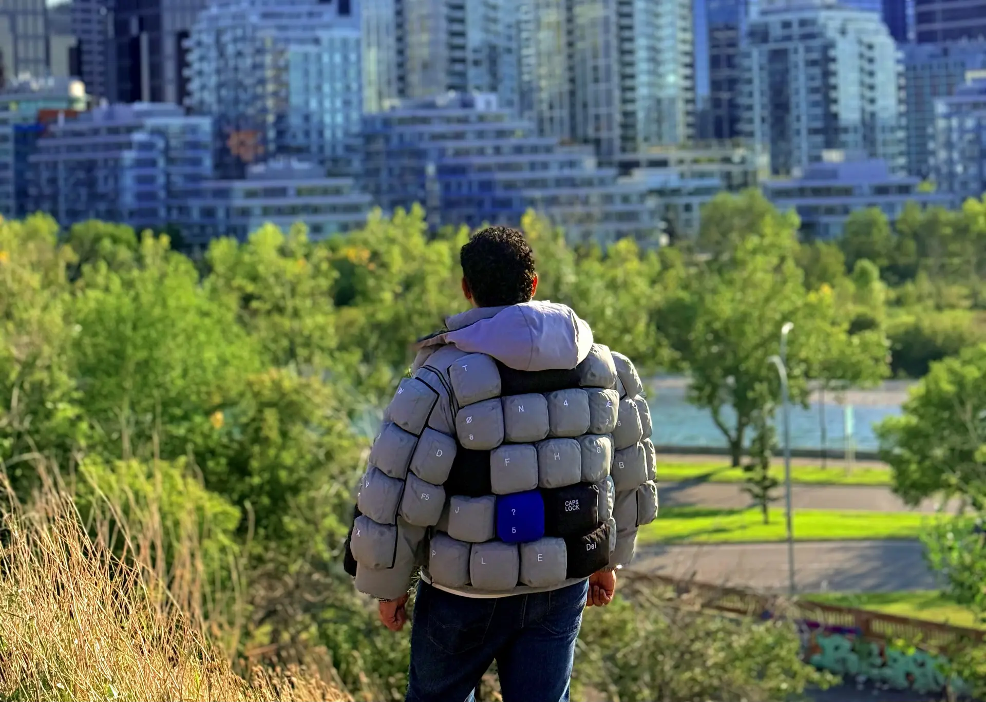 Muhammad faces the Calgary skyline from a green hillside in his keyboard jacket.