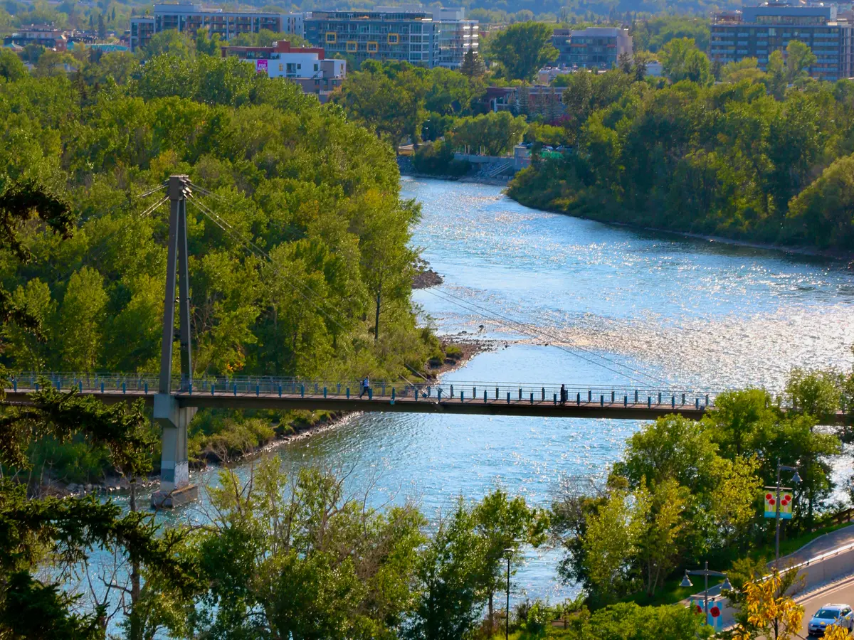 The Bow River and a pedestrian bridge seen from above, downtown Calgary behind.